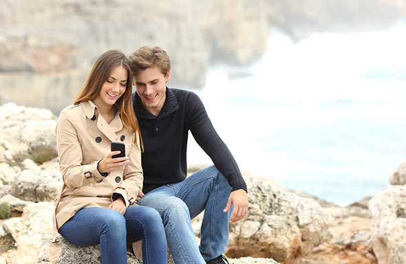 pareja sentada sobre las rocas observando un smartphone